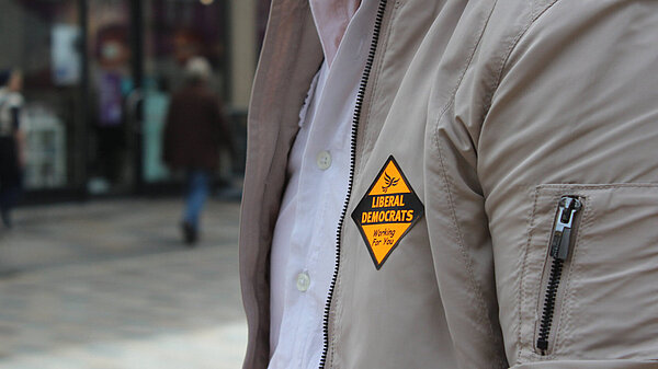 Person wearing a grey jacket with a lib dem sticker on it